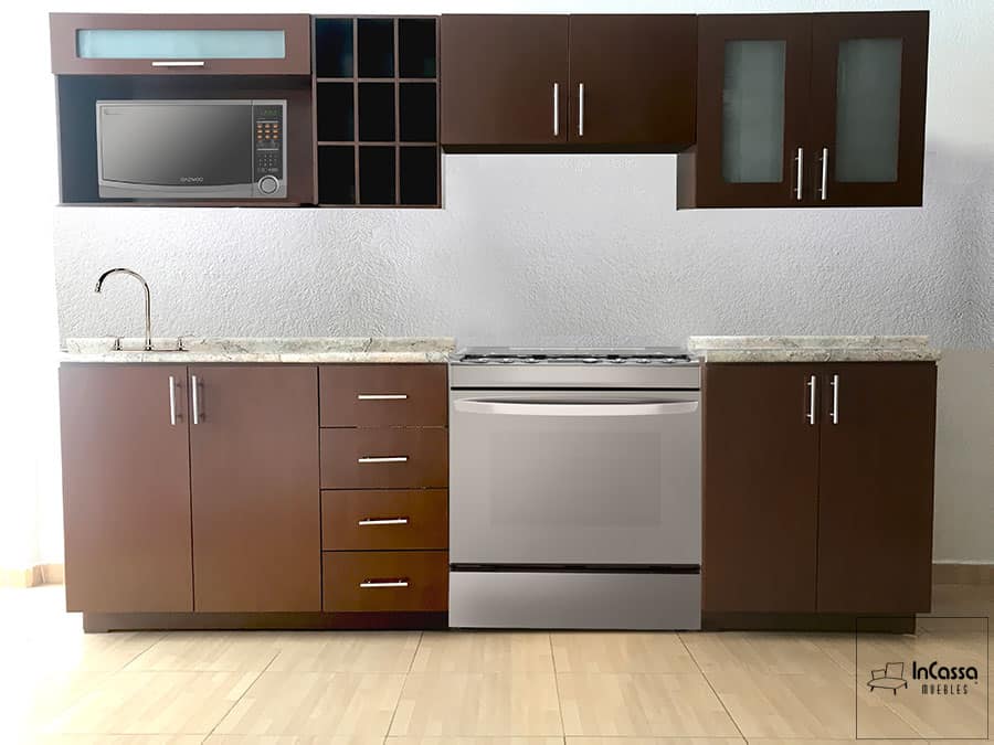 Una toma directa que presenta la distribución lineal de esta elegante cocina. Se observan seis módulos bien distribuidos: alacenas superiores con puertas lisas y de vidrio esmerilado, espacios abiertos para microondas y vinera, además de gabinetes inferiores con cubierta de formaica estilo granito purpina, tarja empotrada y espacio para estufa. Todo en un acabado color tabaco con jaladeras metálicas, ideal para un estilo moderno y funcional.
