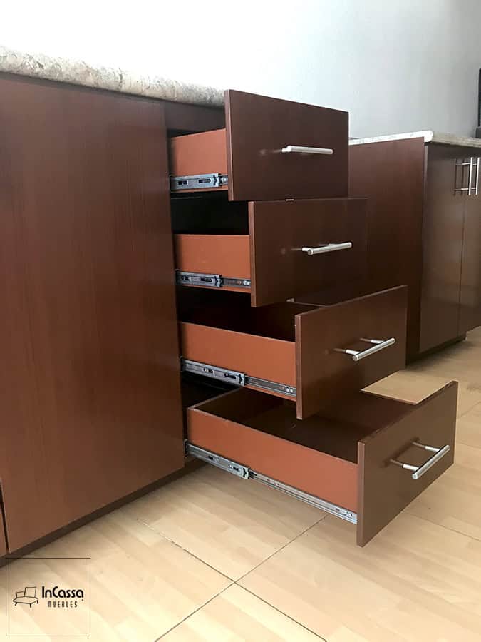 La fotografía muestra un primer plano de los cuatro cajones funcionales en acabado tabaco totalmente abiertos. Se observan las correderas metálicas de extensión y los tiradores alargados, destacando la capacidad de almacenamiento y accesibilidad del módulo.