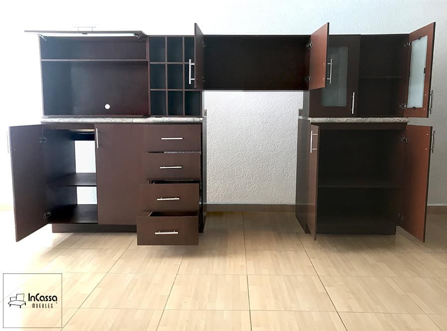 La imagen muestra una toma frontal con todos los compartimentos abiertos en acabado tabaco completo, revelando el amplio espacio de almacenamiento que ofrece este diseño. Se destacan los estantes interiores, las puertas con bisagras de cierre suave, los cuatro cajones funcionales con correderas metálicas y los espacios específicos para microondas y botellas. Una distribución práctica y eficiente que maximiza la organización en cualquier cocina.