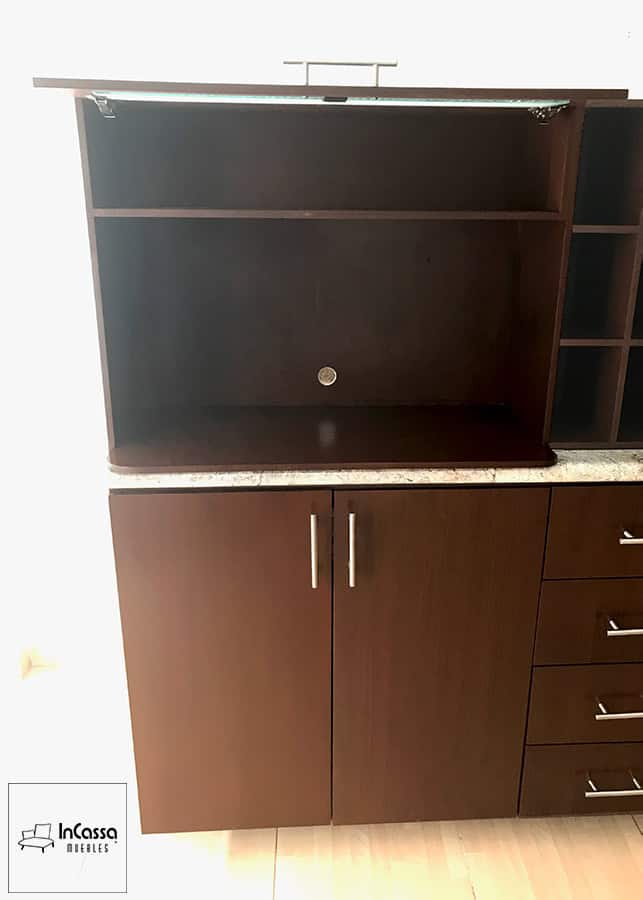 Una toma en primer plano que muestra el módulo superior tabaco abierto, diseñado especialmente para colocar el microondas. Incluye un compartimento adicional en la parte superior y un práctico orificio para cableado, manteniendo el área ordenada. La puerta se eleva fácilmente gracias al soporte neumático de alta calidad.