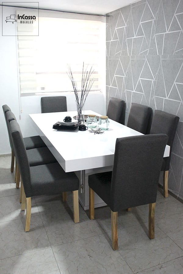 Este elegante comedor de diseño minimalista cuenta con una mesa rectangular blanca de superficie brillante, acompañada de ocho sillas tapizadas en tela pliana gris cátala, con patas de madera de pino, ideal para espacios modernos y sofisticados.