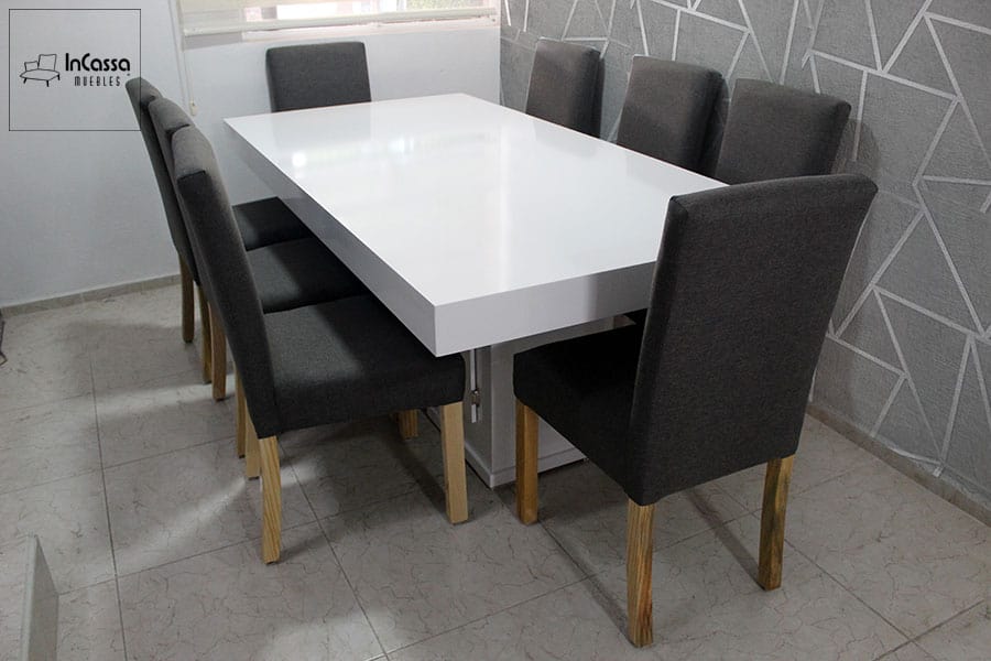 La imagen muestra un comedor para 8 personas contemporáneo compuesto por una mesa rectangular blanca de superficie brillante y sillas tapizadas en pliana gris cátala con patas de madera de pino. Este conjunto es ideal para agregar un toque de elegancia y modernidad a cualquier espacio.