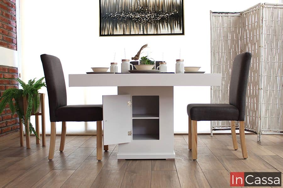 La imagen muestra un comedor con una mesa central blanca completa que destaca por su diseño práctico y moderno. La base de la mesa incluye un compartimento de almacenamiento con puerta, ofreciendo dos niveles de espacio útil para guardar objetos. Este detalle funcional se complementa con el estilo elegante de las sillas tapizadas en lino mouse, creando un ambiente acogedor y contemporáneo.