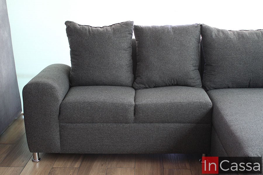 Está imagen se concentra en el love seat de la sala en escuadra, esté cuenta con dos asientos y dos cojines grandes que funcionan como respaldo, además de un amplio descansa brazos; al igual que el chaise long, el love seat está tapizado totalmente en tela lino estilo mouse.