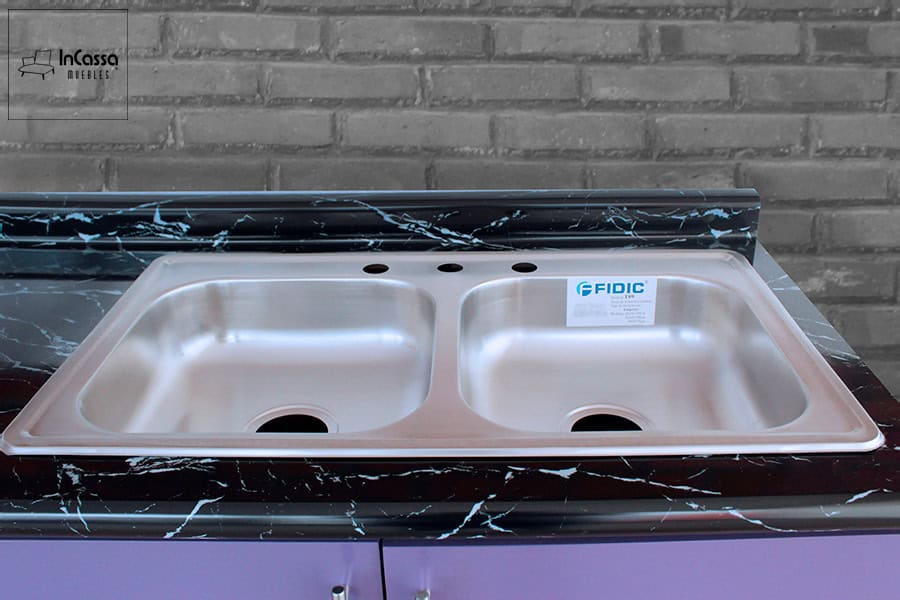 La imagen presenta la tarja doble de acero inoxidable integrada en la Cocina Integral OKAYAMA para parrilla, con cubierta de formaica estilo mármol negro. Su diseño elegante y funcional complementa el acabado color uva, ofreciendo practicidad y durabilidad en el área de lavado.
