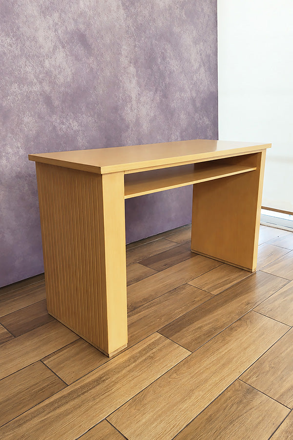 Sin elementos decorativos, esta toma permite apreciar con claridad la estructura del Escritorio estilo Lambrín Modelo ORLEANS en color natural. Destaca su cubierta rectangular, compartimento abierto frontal y panel lateral con acabado acanalado vertical, detalle que aporta textura al diseño.