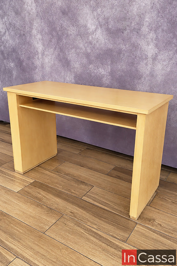 Vista en perspectiva del Escritorio estilo Lambrín Modelo ORLEANS en color natural. Su diseño destaca por una amplia cubierta de trabajo, repisa inferior para organizar accesorios y laterales con detalle acanalado tipo lambrín, que aportan textura y un acabado moderno al mueble.