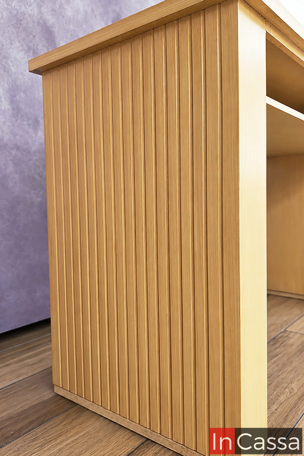 Detalle lateral del Escritorio estilo Lambrín Modelo ORLEANS en color natural. Su costado presenta un acabado acanalado con líneas verticales tipo lambrín, que aporta textura, profundidad y un aspecto contemporáneo, realzando la tonalidad cálida y el acabado tipo madera del mueble.