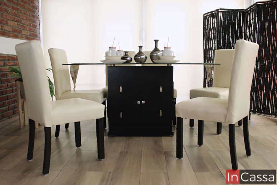 La foto muestra el Comedor Modelo OSLO para 6 personas desde un ángulo frontal, destacando su mesa de cristal templado sostenida por pedestal en color chocolate y sillas tapizadas en tacto piel tono hueso.