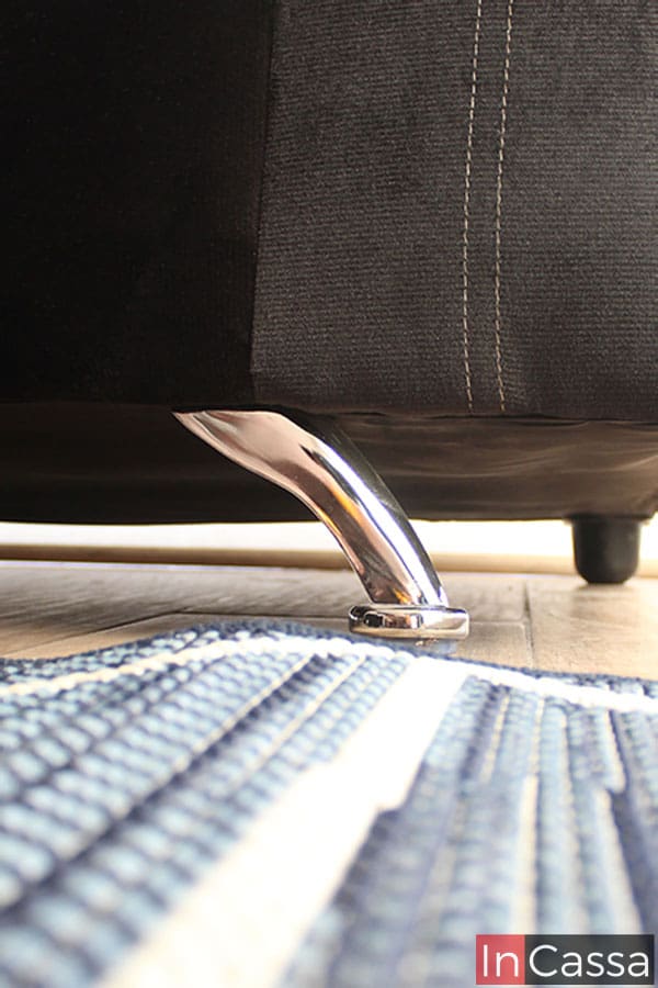 La imagen enfoca las patas que sostienen cada love seat tapizado en suede negro, en la cuál se puede apreciar que las patas delanteras son metálicas y tienen un acabado cromado, mientras que las traseras son más pequeñas de plástico en color café.