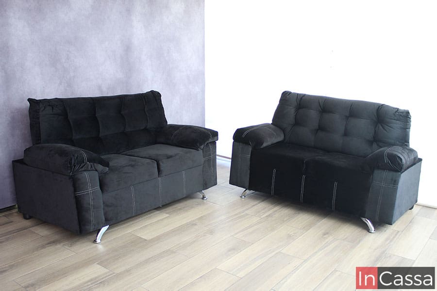 Sala de 2 love seat tapizados en suede negro presentada en una habitación con pared gris y piso de madera.
