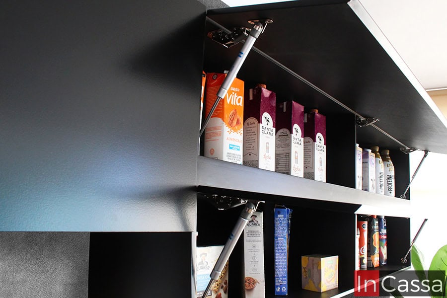 Los módulos superiores de color chocolate de la cocina cuentan con puertas abatibles que incluyen pistones neumáticos, facilitando una apertura suave y cómoda para acceder al almacenamiento superior.