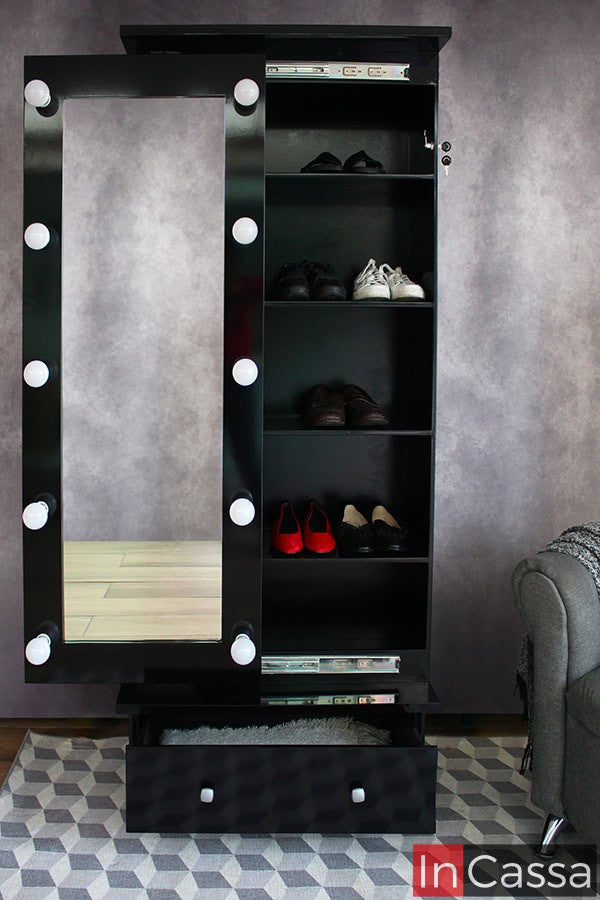 La imagen muestra la zapatera Piacenza en color negro con espejo de cuerpo completo y marco con bombillas LED apagadas. La puerta está abierta revelando repisas internas que almacenan varios pares de zapatos y una sección inferior con cajón extraíble de tiradores cuadrados.