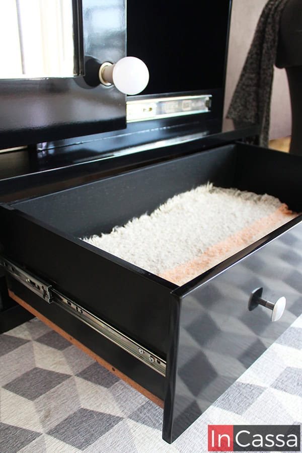 Vista en primer plano del cajón inferior de la zapatera Piacenza en acabado negro brillante, abierto para mostrar su interior forrado con alfombra suave en tono claro. Se observan correderas metálicas de extensión y un tirador cuadrado en color plateado.