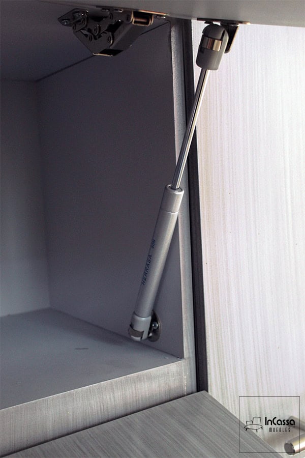 La imagen muestra un acercamiento al pistón neumático instalado en el módulo superior de la cocina PISA para Estufa en color gris cenizo claro. Este herraje de alta calidad garantiza una apertura suave y segura, brindando durabilidad y confort en el uso diario. Ideal para quienes buscan funcionalidad y practicidad en cada detalle.