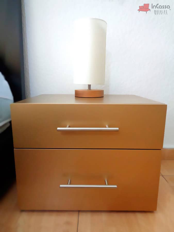 En esta imagen se muestra de frente un buró del modelo Portugal, acabado en tono maple y equipado con dos amplios cajones con jaladeras metálicas. Encima destaca una lámpara de base redonda que complementa perfectamente el diseño moderno del mueble.