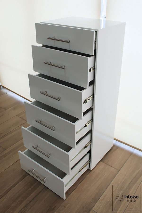 La imagen presenta una vista superior lateral de la cajonera vertical en acabado blanco brillante, exhibiendo sus seis cajones completamente abiertos. Se aprecian los rieles metálicos de extensión y las jaladeras modernas, destacando su funcionalidad y estilo limpio.