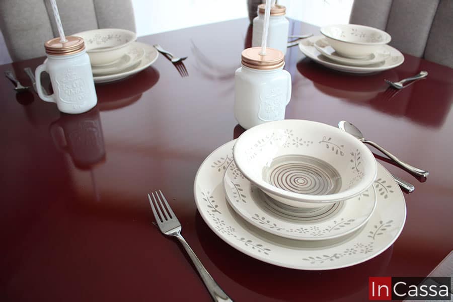 La foto se concentra en mostrar la cubierta de la mesa, en la cual destaca el acabado brillante de la pintura borgoña gracias a las vajillas y utensilios que decoran la cubierta, de las cuales es posible observar su reflejo en la superficie.