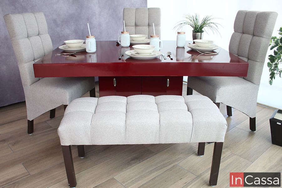 En está foto tenemos una vista frontal de la mesa color borgoña así como de la banca tapizada en lino greige, al igual que una toma lateral de las sillas tapizadas en la misma tela y color, además de que las patas color café quedan resaltadas gracias al piso de madera.