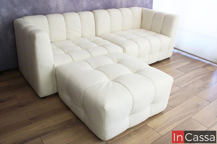 Se observa la Sala tipo NUBE Modular Modelo RODAS tapizada en suede hueso, presentada en una elegante configuración con otomán independiente que brinda gran versatilidad para adaptarse a diferentes espacios y necesidades. Su diseño de líneas redondeadas, respaldos envolventes y amplios cojines acolchados crea una apariencia contemporánea y sofisticada, mientras que el tapizado en tono hueso aporta luminosidad y una sensación de amplitud al ambiente.