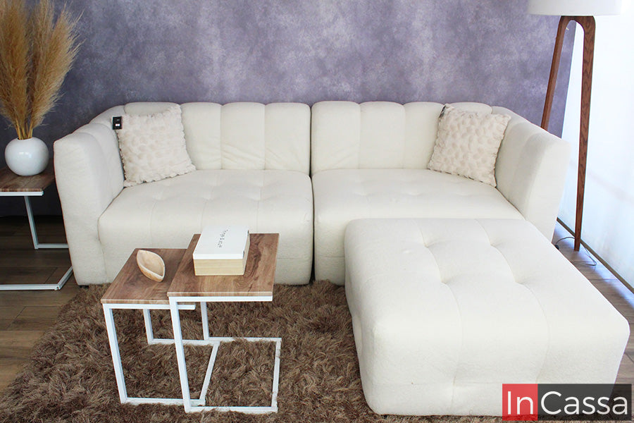 En esta toma frontal se aprecia la sala modular tipo nube Modelo RODAS en suede color hueso, con diseño capitoneado y líneas suaves; su módulo tipo chaise aporta mayor confort, mientras las mesas auxiliares y tonos cálidos crean un ambiente elegante y acogedor.