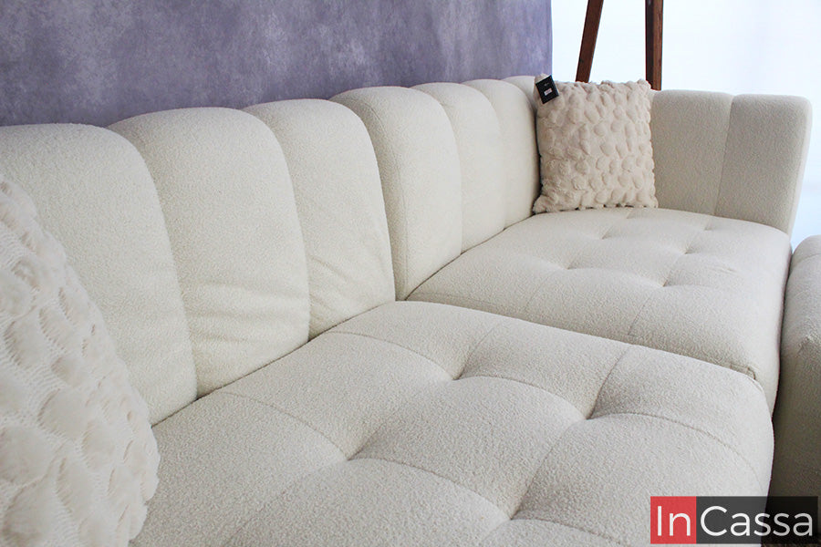 Un acercamiento lateral destaca la sala modular RODAS en suede color hueso, mostrando su capitoneado uniforme y textura suave; sus líneas curvas y respaldo acolchado brindan confort envolvente, ideal para crear espacios cálidos, modernos y altamente acogedores.
