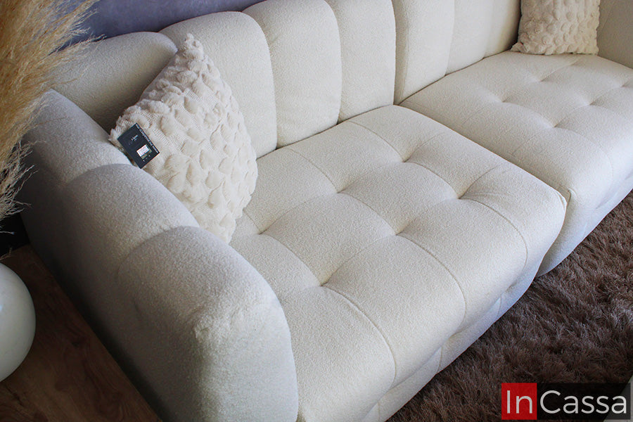 La imagen muestra un acercamiento en ángulo de la sala modular RODAS en suede color hueso, resaltando su capitoneado profundo y textura suave; sus brazos redondeados y cojines decorativos aportan un estilo elegante, moderno y sumamente confortable.