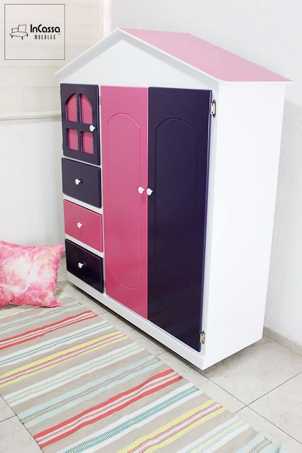 La imagen presenta el Roperito Infantil Modelo ROMINA, diseñado en forma de casita con estructura blanca y detalles en rosa pastel y uva. Su encantador diseño combina tres cajones inferiores, una puerta con ventana decorativa y dos puertas amplias superiores, perfecto para mantener orden y color en la habitación infantil.