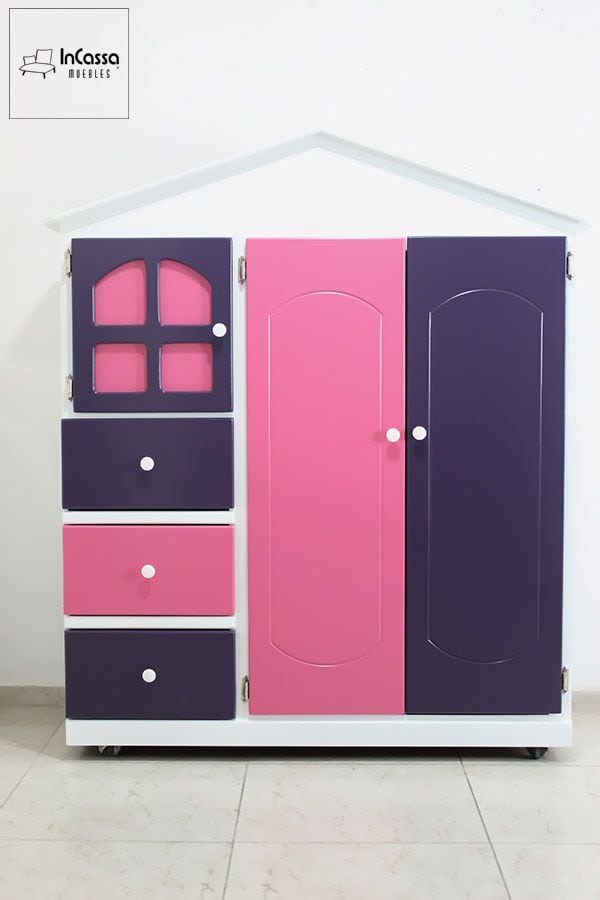 La imagen presenta el Roperito Infantil Modelo ROMINA en una encantadora vista frontal, con estructura blanca y diseño de casita. Sus puertas y cajones en tonos rosa pastel y uva crean un contraste alegre y moderno, ideal para habitaciones infantiles llenas de color y estilo.