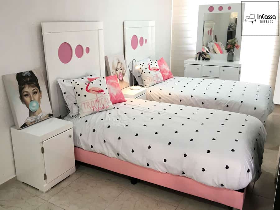 La imagen muestra camas individuales con cabeceras blancas y detalles rosados, acompañadas de buroes blancos y un tocador que complementan un dormitorio armonioso y funcional.