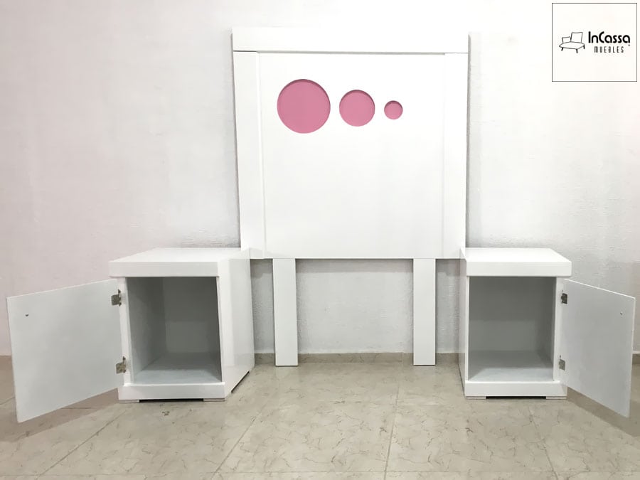 La imagen muestra una cabecera blanca con detalles circulares en rosa y dos burós blancos abiertos con puertas. Su diseño práctico y moderno es ideal para dormitorios juveniles.