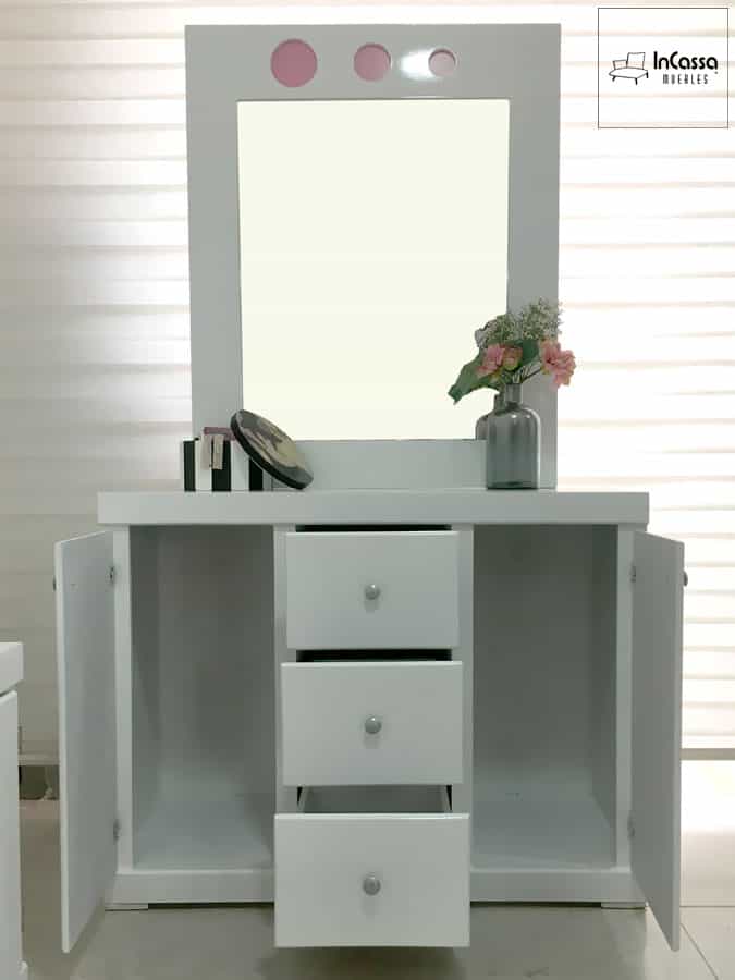 Se presenta un tocador blanco completo con espejo integrado y detalles circulares en rosa. Sus cajones y compartimentos abiertos ofrecen amplio espacio para organizar tus pertenencias.