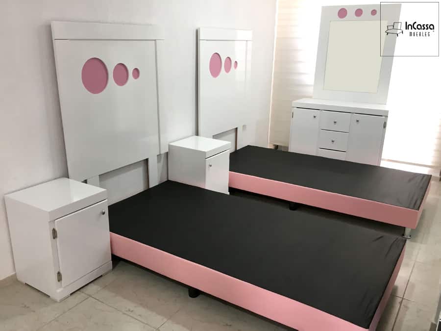 Una toma de dos bases de cama individuales en negro con bordes rosados, combinadas con cabeceras blancas con detalles rosados y buroes blancos, resaltando un estilo minimalista y moderno.