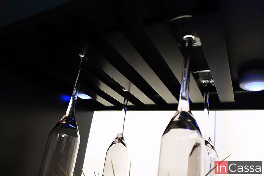 La imagen muestra una vista inferior del portacopas de la cantina ROSWELL, destacando sus ranuras de madera en color chocolate y la elegante iluminación LED. Las copas colgantes crean un efecto visual moderno y funcional, ideal para exhibición y fácil acceso.