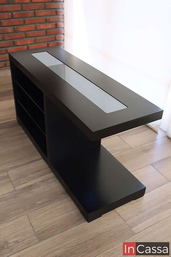 La imagen muestra una toma en ángulo superior donde se aprecia el diseño limpio y moderno de la cantina ROSWELL, con cubierta en acabado chocolate y detalle central en cristal. Su estructura simétrica y base ancha aportan estabilidad y elegancia al mueble.