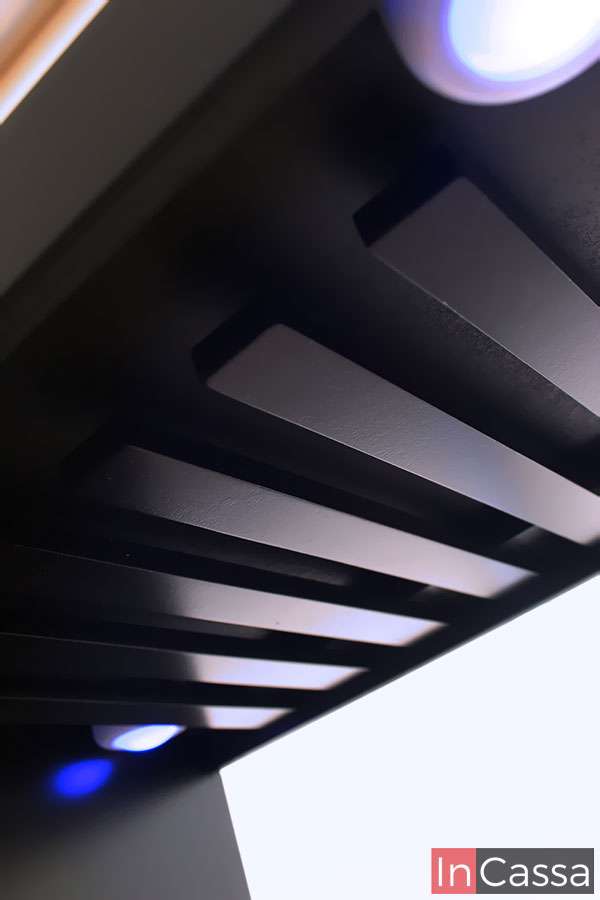 Una toma cerrada desde abajo revela el diseño del portacopas de la cantina ROSWELL, compuesto por listones de madera en acabado chocolate mate. La iluminación LED en tonos fríos destaca la modernidad del mueble y mejora la visibilidad en espacios con poca luz.