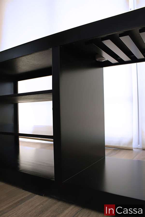 La imagen muestra una perspectiva inferior lateral del mueble cantina ROSWELL, donde se aprecian sus repisas abiertas y el sistema de portacopas integrado. El acabado en chocolate mate realza su diseño moderno y funcional, ideal para optimizar espacios reducidos con estilo.