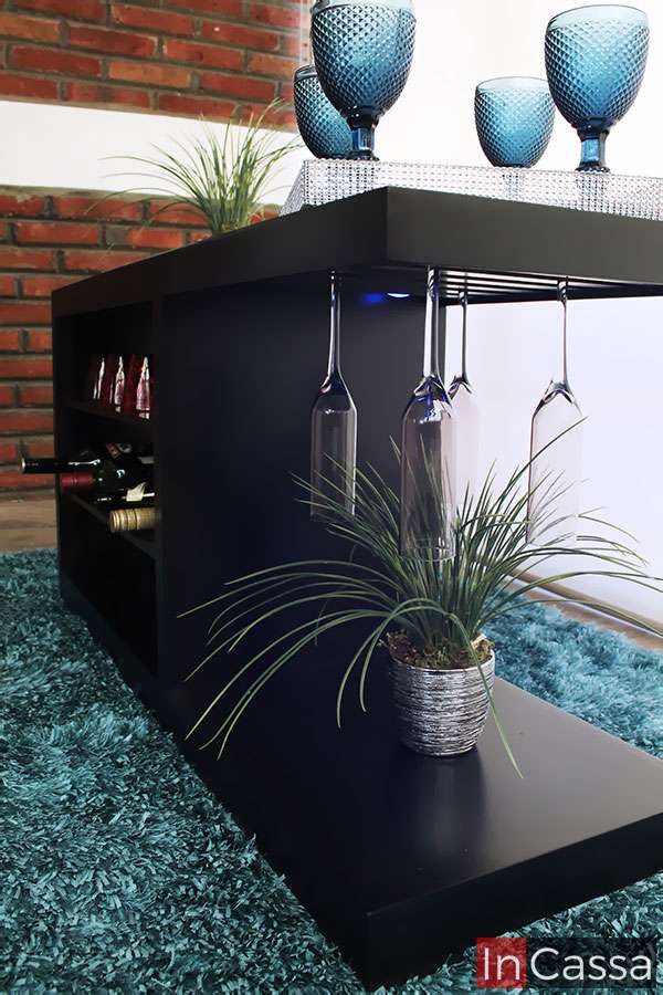 La foto muestra una vista lateral desde ángulo bajo de la cantina ROSWELL en acabado chocolate. Se destaca el práctico portacopas colgante iluminado con luz LED, además del entrepaño decorativo inferior y la cava lateral para botellas.