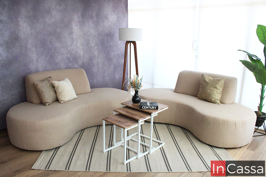 La imagen presenta la Sala Redonda Modelo SALÓNICA con diseño orgánico y líneas suaves, tapizada en suede gris perla. Sus módulos curvos crean un ambiente moderno, armonioso y acogedor, complementado con mesas laterales y decoración minimalista.