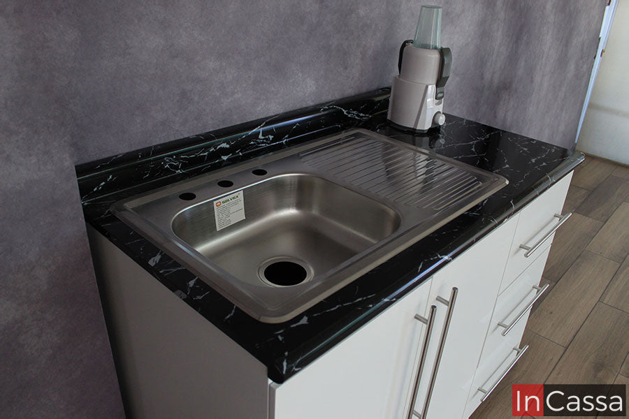 Enfocamos el modulo de tarja, mostrando que la cocina incluye una tarja de acero inoxidable con escurridor, la cuál ya se encuentra empotrada en la cubierta de formica en color mármol negro.