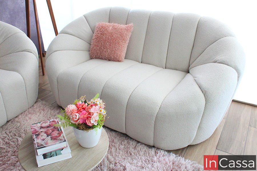 En esta toma lateral, la sala SAMARA luce sus curvas orgánicas y acolchado vertical que refuerzan su estética tipo nube; el suede color hueso aporta calidez y sofisticación, mientras los cojines en tonos rosados complementan un ambiente dulce, moderno y acogedor.