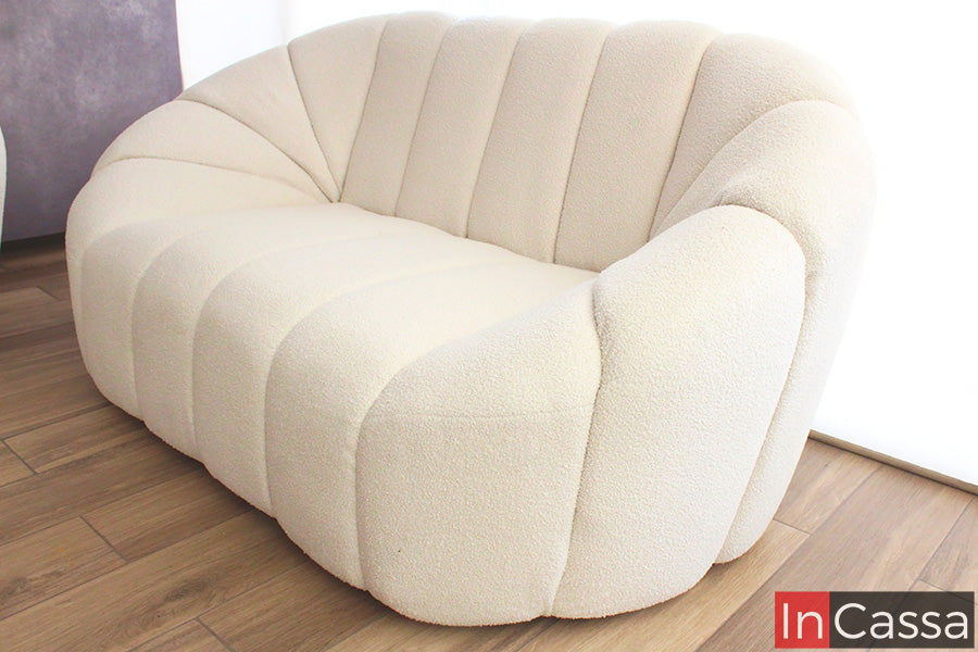 Una toma en ángulo frontal que resalta el volumen orgánico de la sala SAMARA; sus curvas continuas y capitoné vertical en suede color hueso crean una pieza visualmente fluida, elegante y sumamente acogedora, ideal para espacios modernos y luminosos.