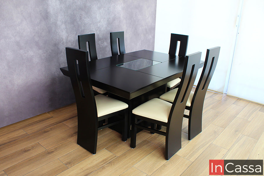 La foto muestra el elegante diseño del comedor en su presentación completa. Destaca la estructura robusta de la mesa con cubierta chocolate y arenero central decorativo acompañada por seis sillas de respaldo alto y asiento tapizado en suede hueso.