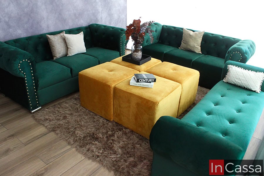 Una toma cenital presenta el modelo San Petersburgo en tres módulos separados: dos sofás y un diván en suede verde botella. Al centro, cuatro taburetes en suede dorado sobre tapete, con capitoneado y patas cromadas.