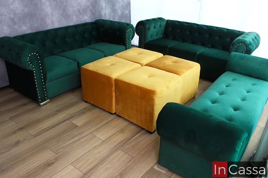 La foto muestra la sala San Petersburgo completa: dos sofás y un diván en tapizado suede verde botella, acompañados por cuatro taburetes en suede dorado. Su diseño capitoneado y remaches dorados crean un estilo elegante y moderno.