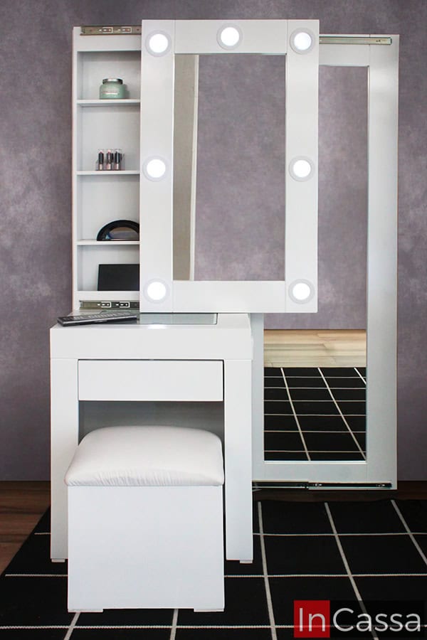 Se presenta el Tocador Vanity Santorini en acabado blanco, con espejo principal de 7 focos LED encendidos y estantes internos ocultos, además de un espejo lateral de cuerpo completo. La foto resalta el diseño minimalista y la funcionalidad del mueble desde un ángulo frontal.