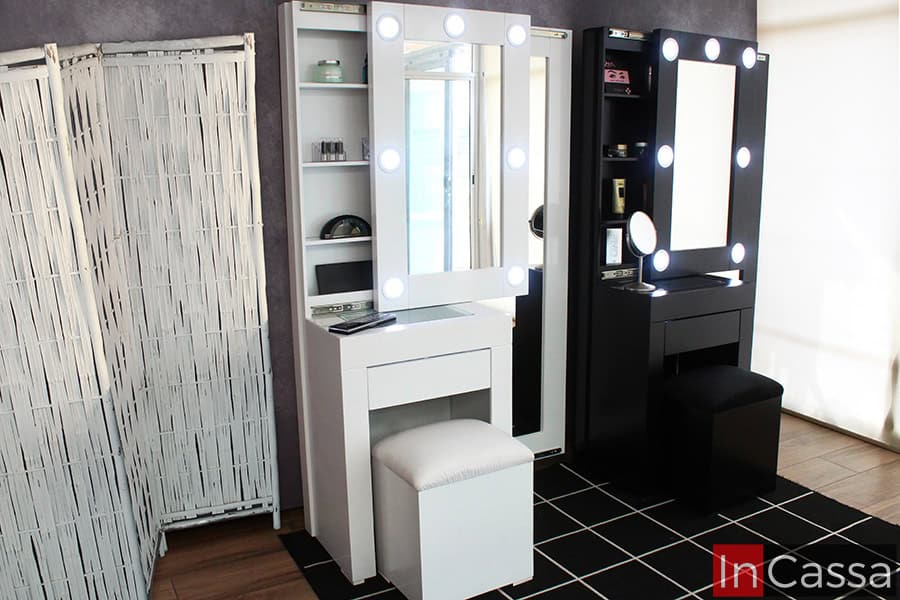 La imagen muestra dos Tocadores Vanity Santorini, uno en blanco y otro en negro, ambos con espejos iluminados por 7 focos LED. Se aprecian sus estantes internos y bancos acolchados, además de sus espejos laterales de cuerpo completo, resaltando diseño y funcionalidad en conjunto.