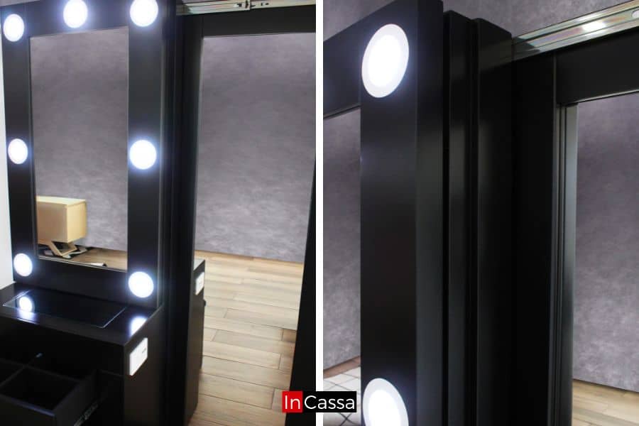 Una toma cercana muestra el sistema de iluminación LED en el espejo del tocador Santorini negro. Se aprecia el diseño elegante con cajones organizadores abiertos y estructura lateral en acabado mate.