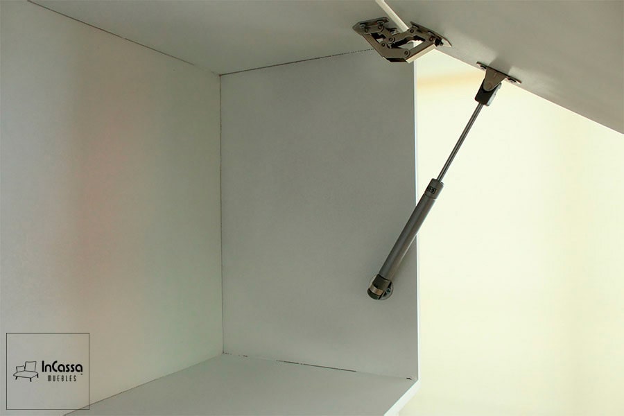 Una toma enfocada en el interior del módulo sobre campana, en el cuál se mantiene el mismo color blanco que en los exteriores del mueble. Además destacan el pistón neumático y la bisagra metálica integrados a la estructura de módulo, ofreciendo un sistema de apertura y cierre vertical.