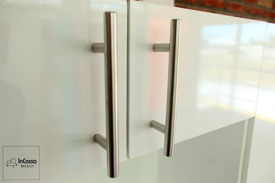 La imagen se concentra en las jaladeras integradas a las puertas de la alacena superior, siendo estás metálicas con estilo de barra T. La toma también resalta el acabado brillante de la alacena blanca.